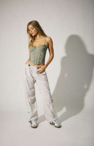Model is wearing a corset, and grey parachute pants.