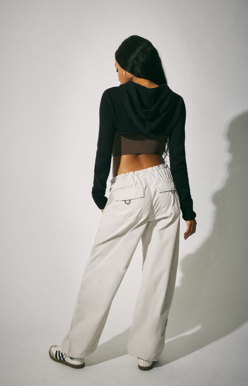 A model wears a shrug, corset top, and white parachute pants.