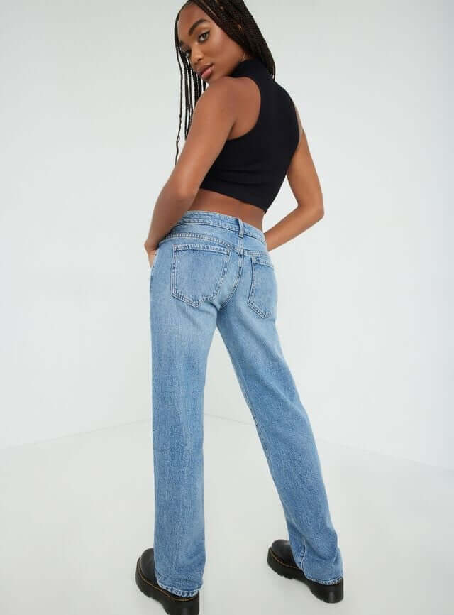 Model is wearing a black tank top and low rise medium wash jeans.