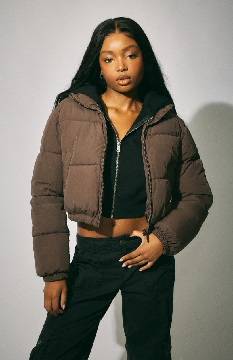 Model wears a puffer coat over a black hoodie with black pants.