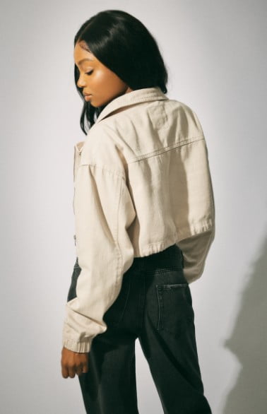 Model wears a white jacket with a black top and dark jeans.