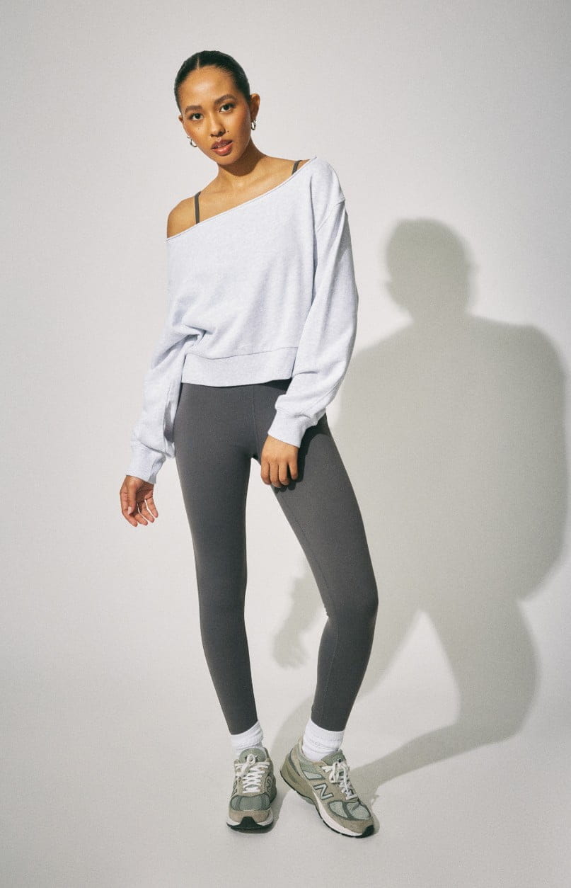 Model wears a grey off the shoulder sweater and black sweats.