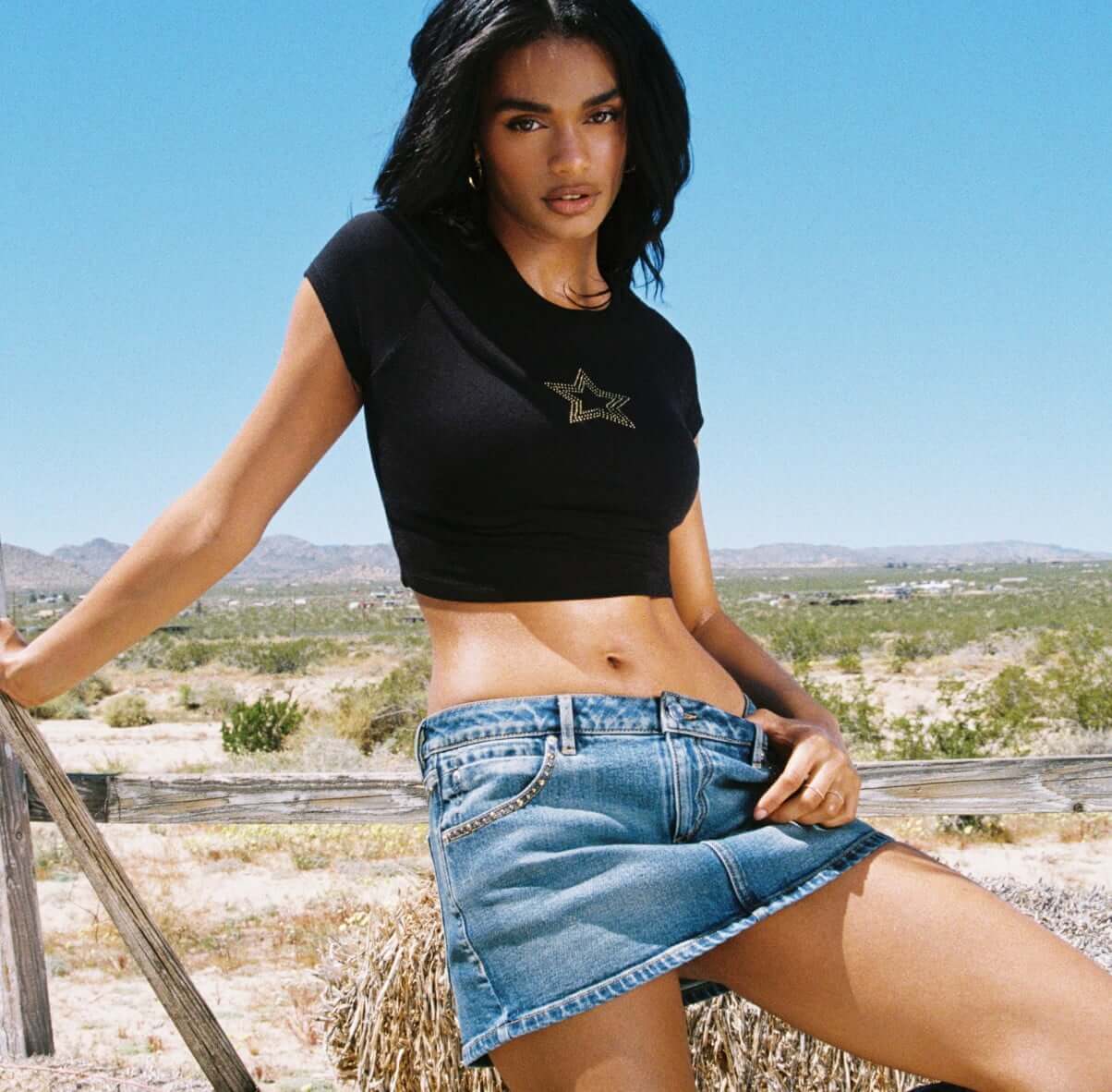Model poses in a black cropped graphic tshirt and denim mini skirt.