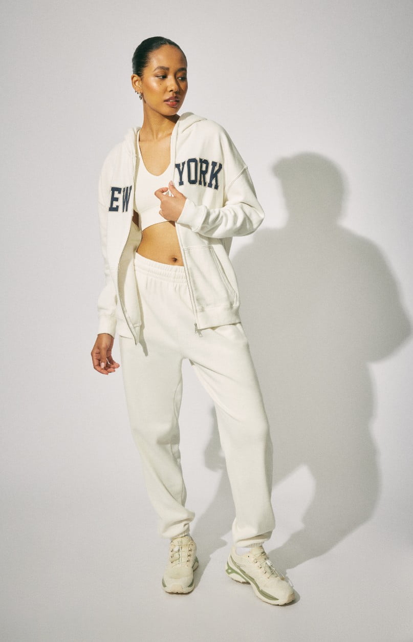 Le mannequin porte un haut à capuchon blanc « New York » avec un jogging blanc.