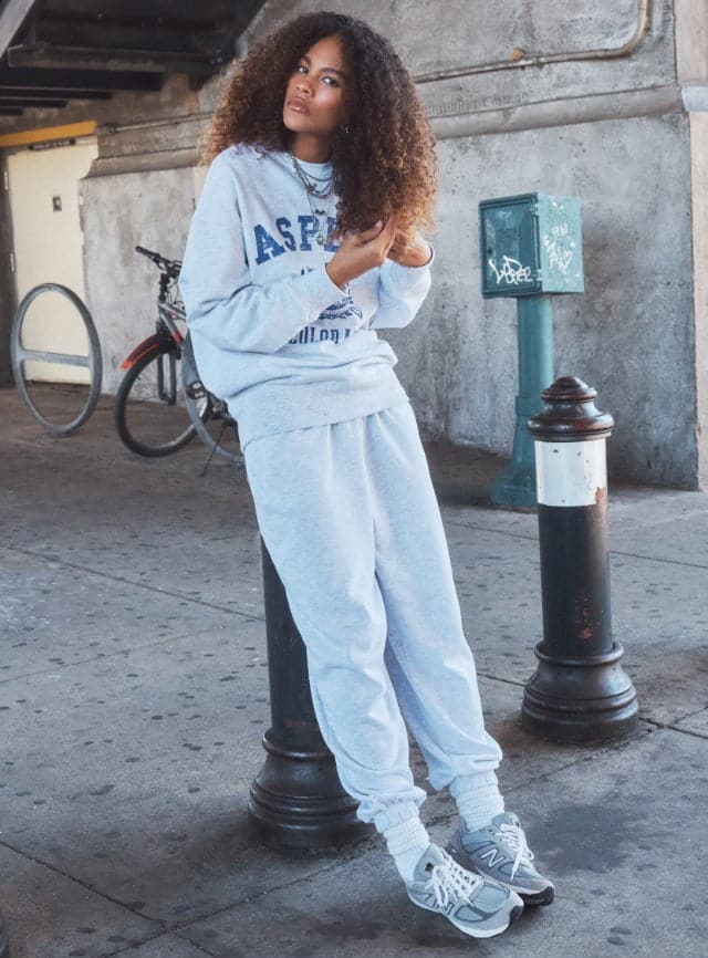 Model is wearing a grey sweatshirt and matching grey joggers.