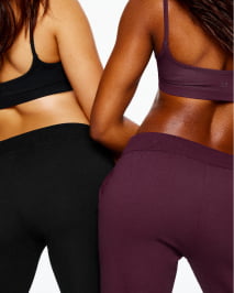 Two models pose in matching sports bras and pants, one in black, the other in burgundy.