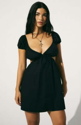 Model is wearing a black mini dress with puff sleeves and cut-out detailing.