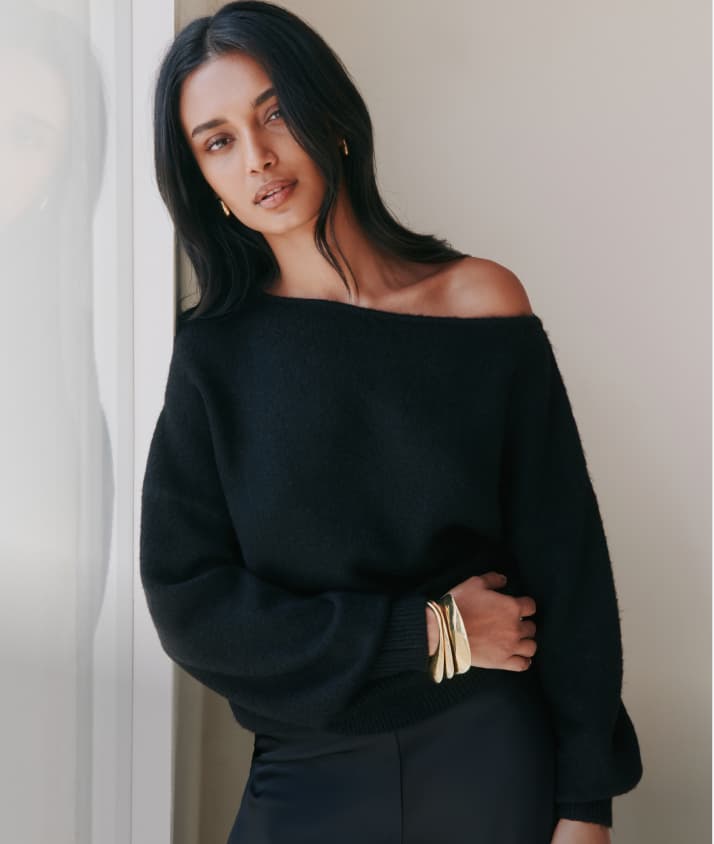 Model is wearing a black off shoulder sweater and black pants.