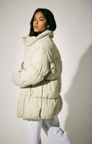 Model is wearing a beige puffer, white top, and fleece bottoms.