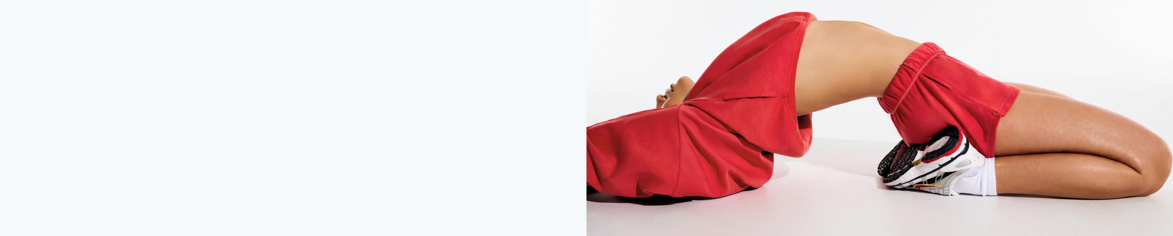 Model poses in a red hoodie and red fleece shorts.