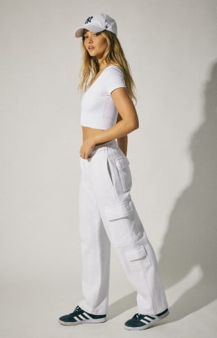 Model is wearing white fleece bottoms, a white crop top, and a logo hat.