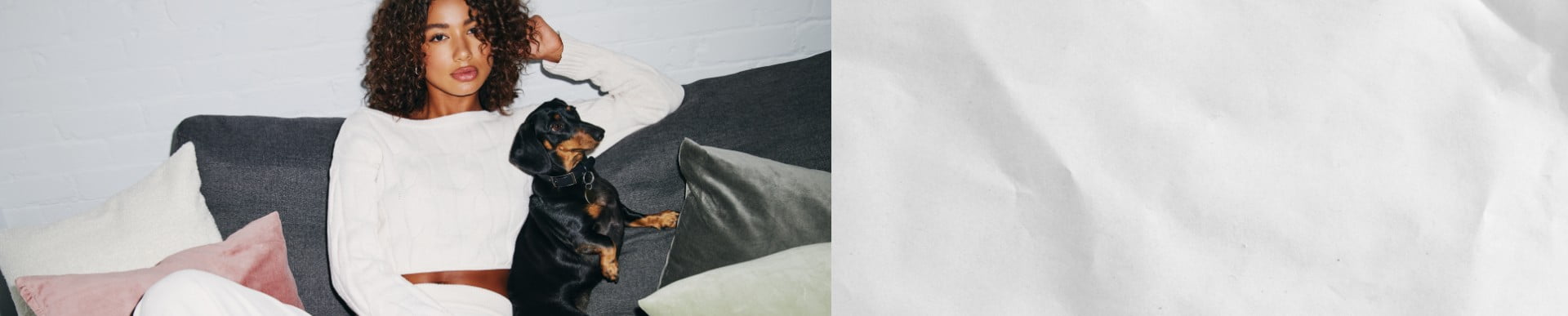 Model poses in a white sweatsuit with a dog in her lap.