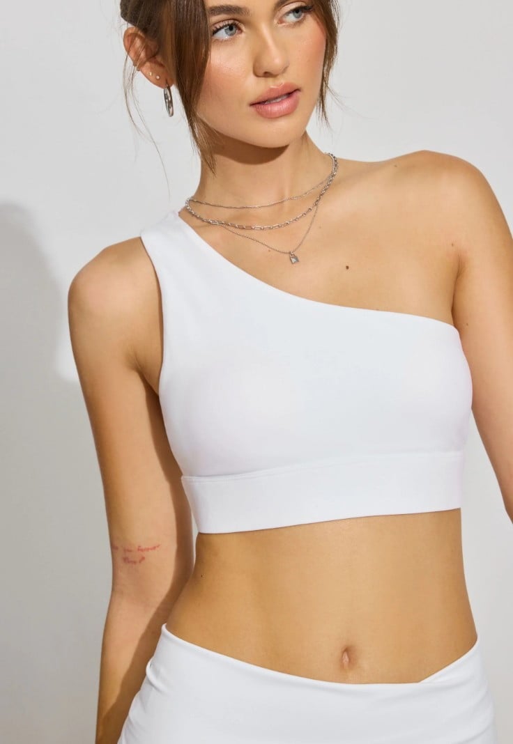 Model wears a white tank top with one strap and white shorts.