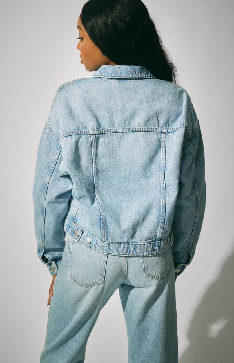 Model wears a denim jacket, denim corset, and jeans.