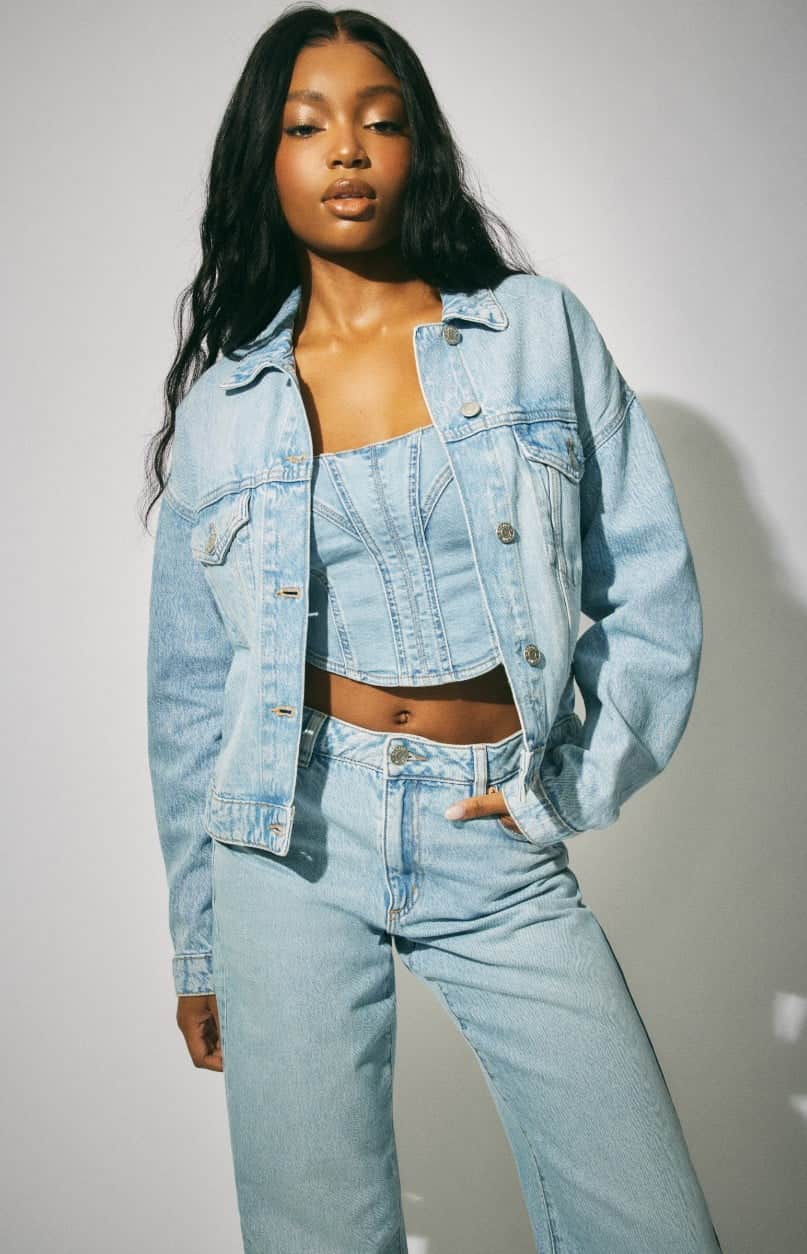 Model wears a denim jacket, denim corset, and jeans.