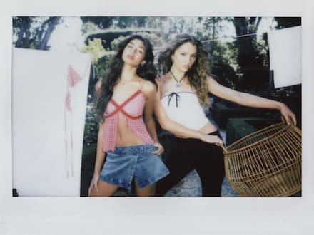 First model wears a red and pink shirt and a denim mini skirt. The second wears a white tube top with a black trim and black pants.