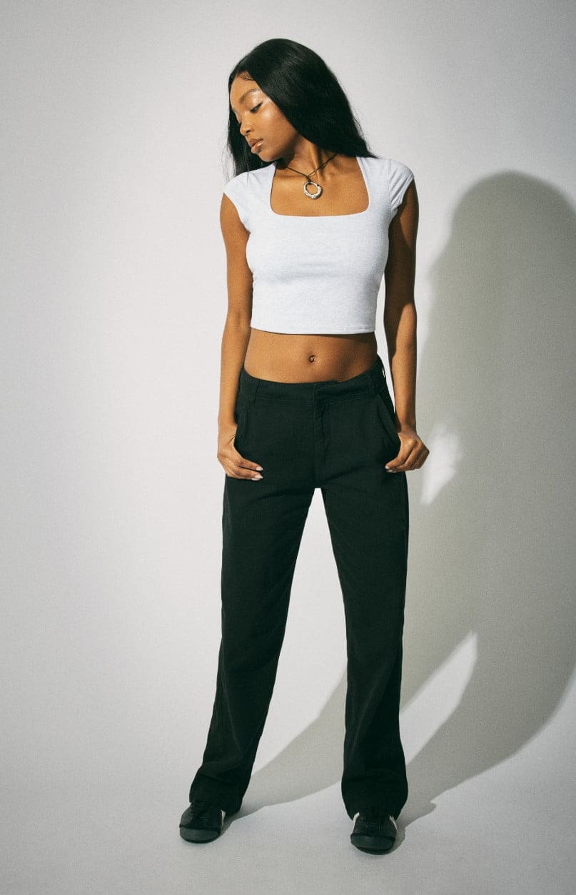 Model poses in a cropped grey tshirt and black trousers.