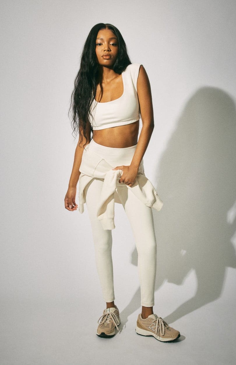 Model wears a cropped white tee with white leggings and a white sweater around her waist.