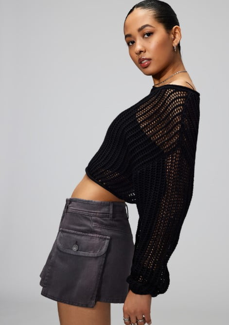 Model poses in a black knit sweater and a grey skirt.