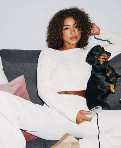 Model poses in a white sweater and white sweater pants.