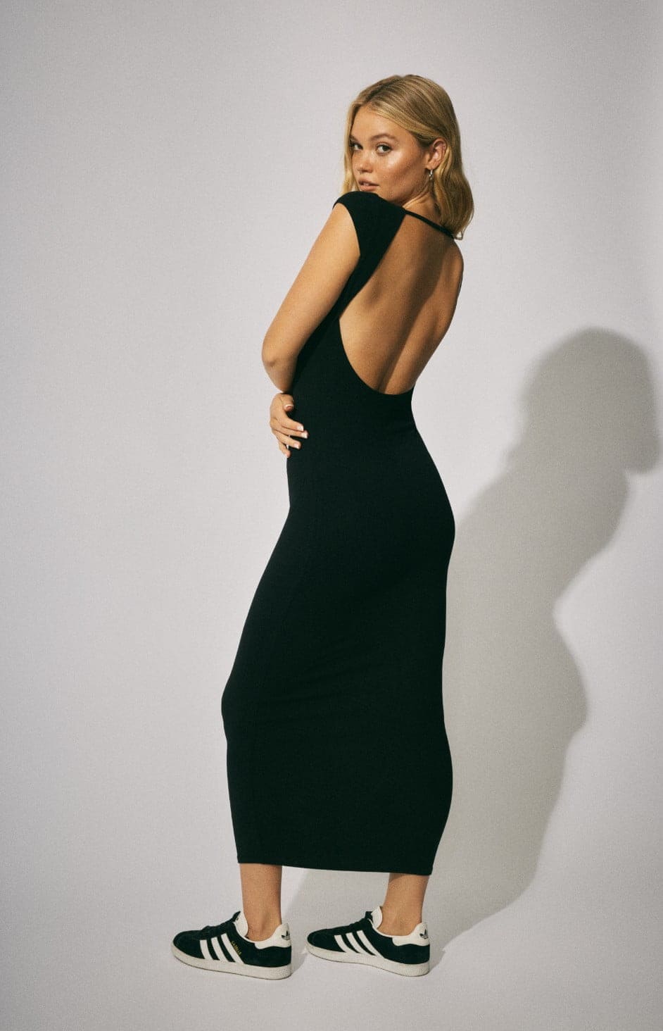Model wears a backless black maxi dress.