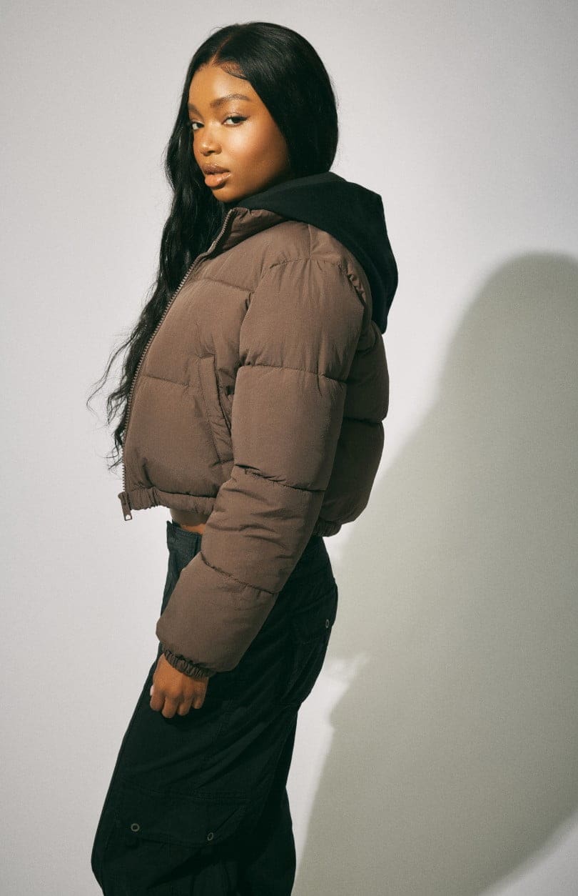 Model wears a puffer coat over a black hoodie with black pants.