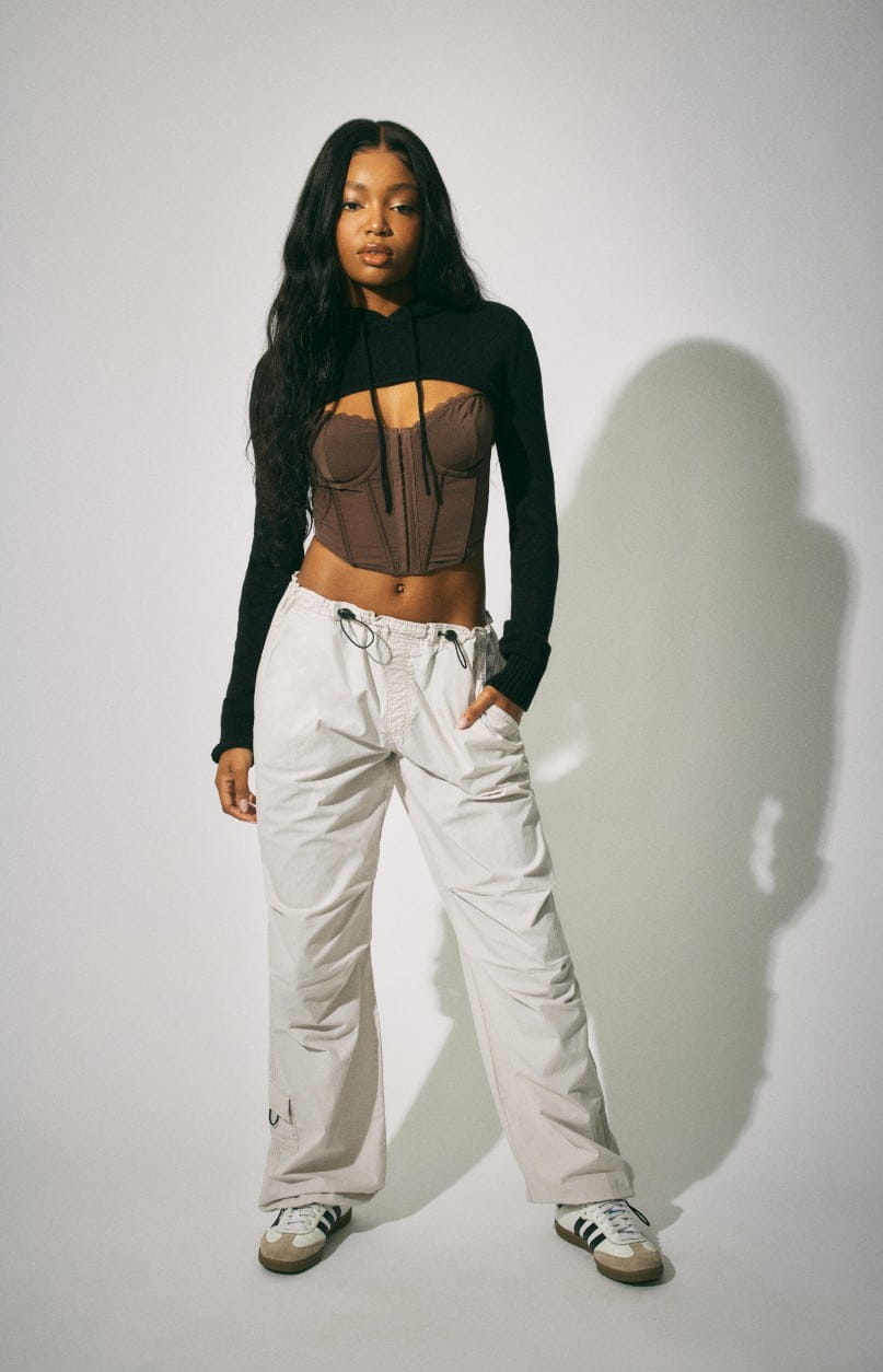 A model wears a shrug, corset top, and white parachute pants.