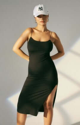 Model is wearing a black midi dress with spaghetti straps and a slit.
