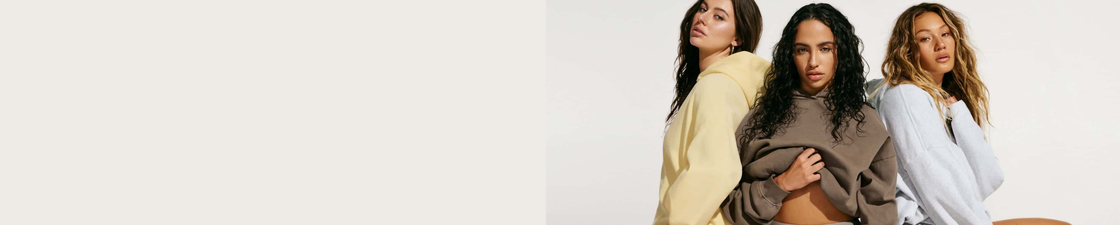 Three models wear hoodies and active shorts, one in light yellow, another in taupe, and the last in white.