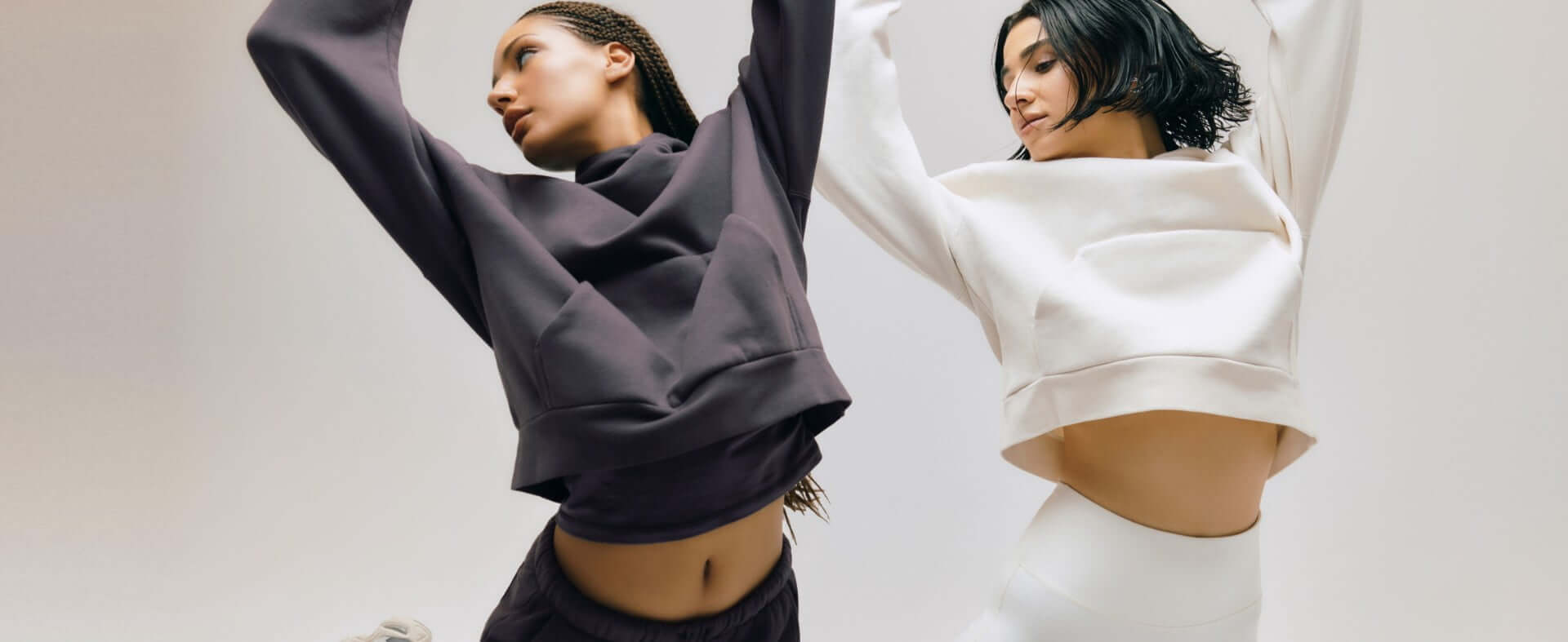 Models poses in matching sweatsuits, one in dark grey and the other in white.