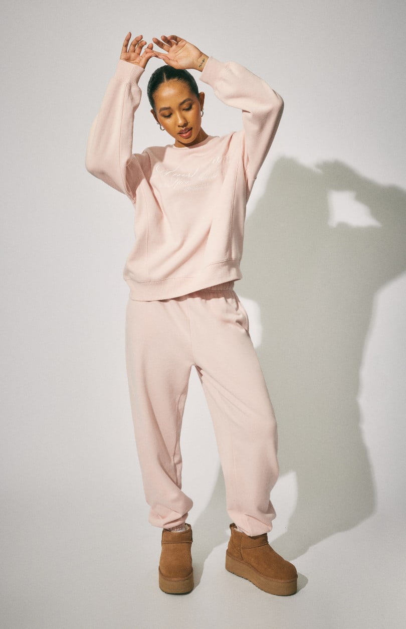 Model wears a pink sweat shirt with matching sweatpants.
