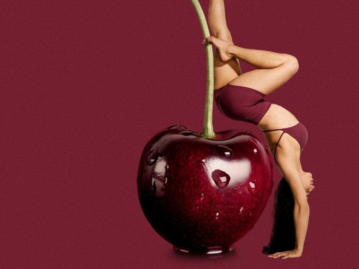 Model poses against a giant cherry wearing dark a red active top and matching shorts.