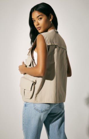 Model is wearing a cargo vest, white tank top, and blue denim.