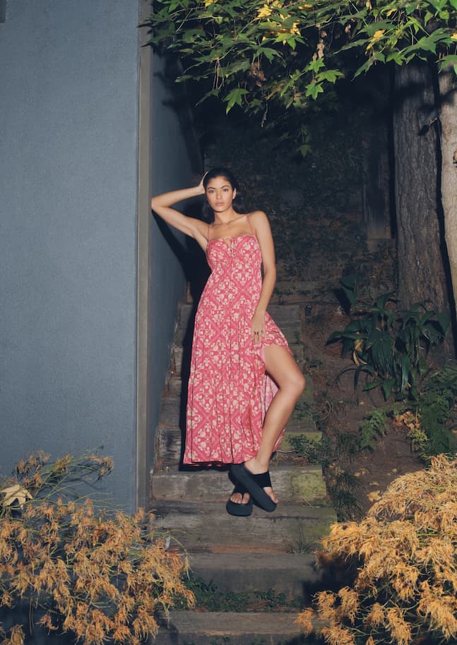 A model wears a pink printed maxi dress with a leg slit.