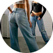 Model poses in jeans and a white lace top with another model in a black corset, black cardigan, and jeans.