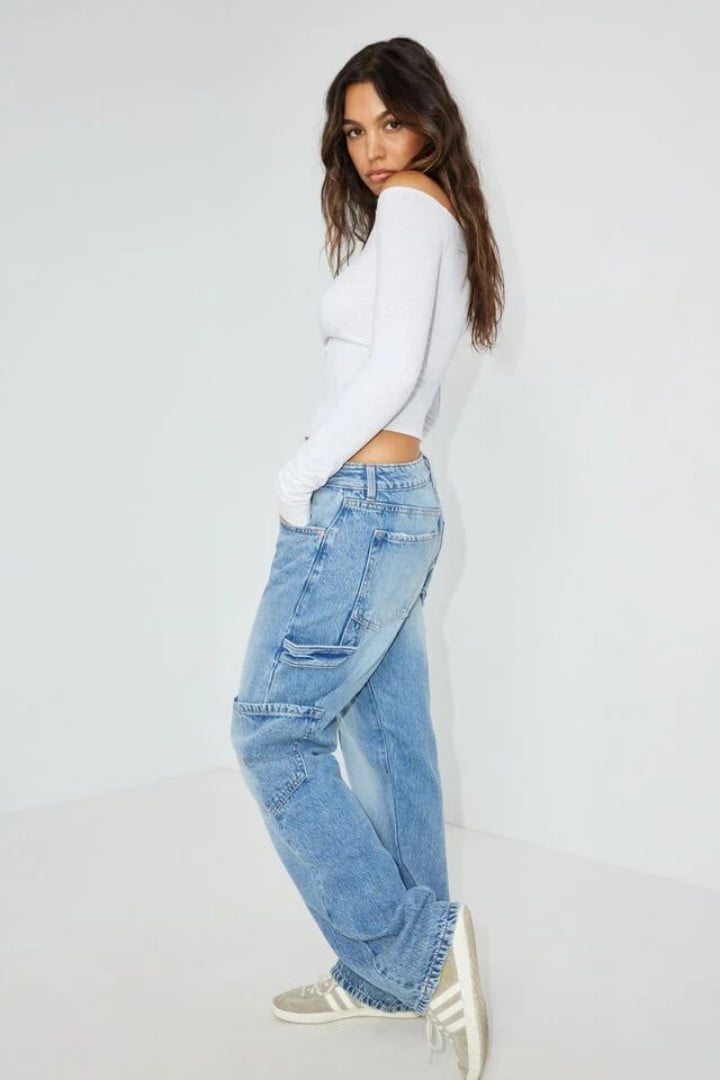 Model wears a white off the shoulder long sleeve shirt and jeans.