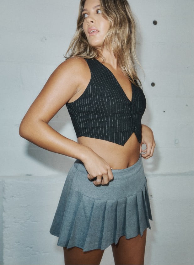 Model is wearing a vest and a pleated skirt.