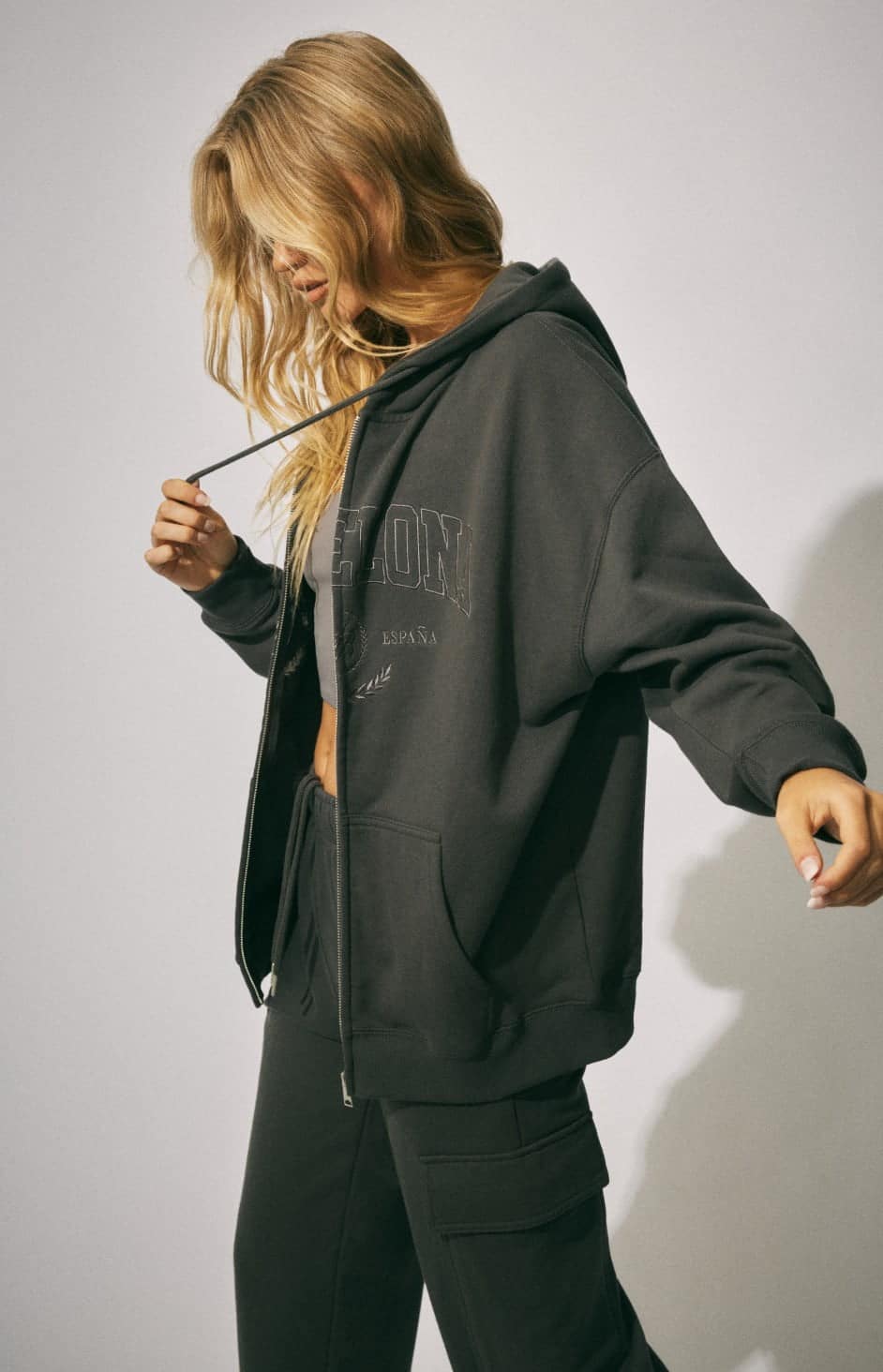 Model wears a hoodie with a grey tank top and black pants.
