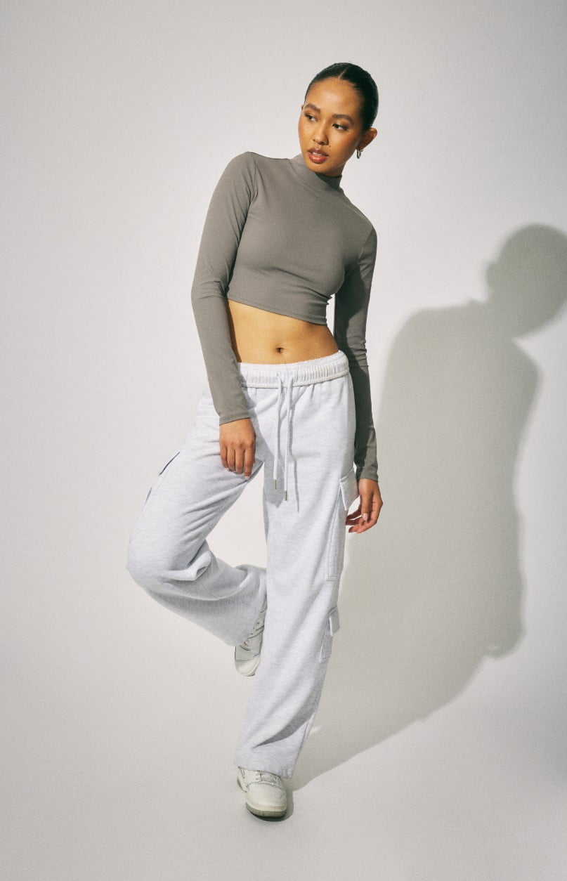 Model wears a cropped long sleeve shirt and grey joggers.