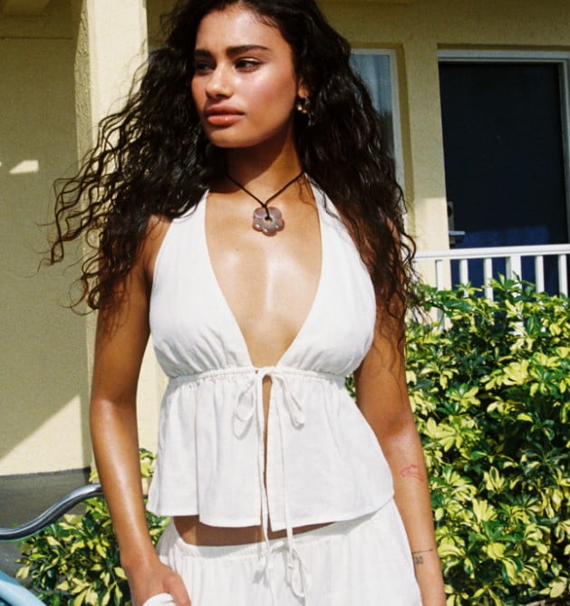 Model poses in a white halter top with matching white pants.