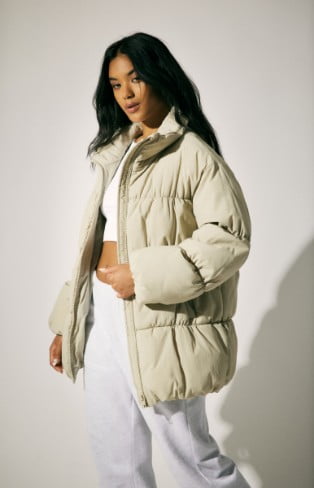 Model is wearing a beige puffer, white top, and fleece bottoms.