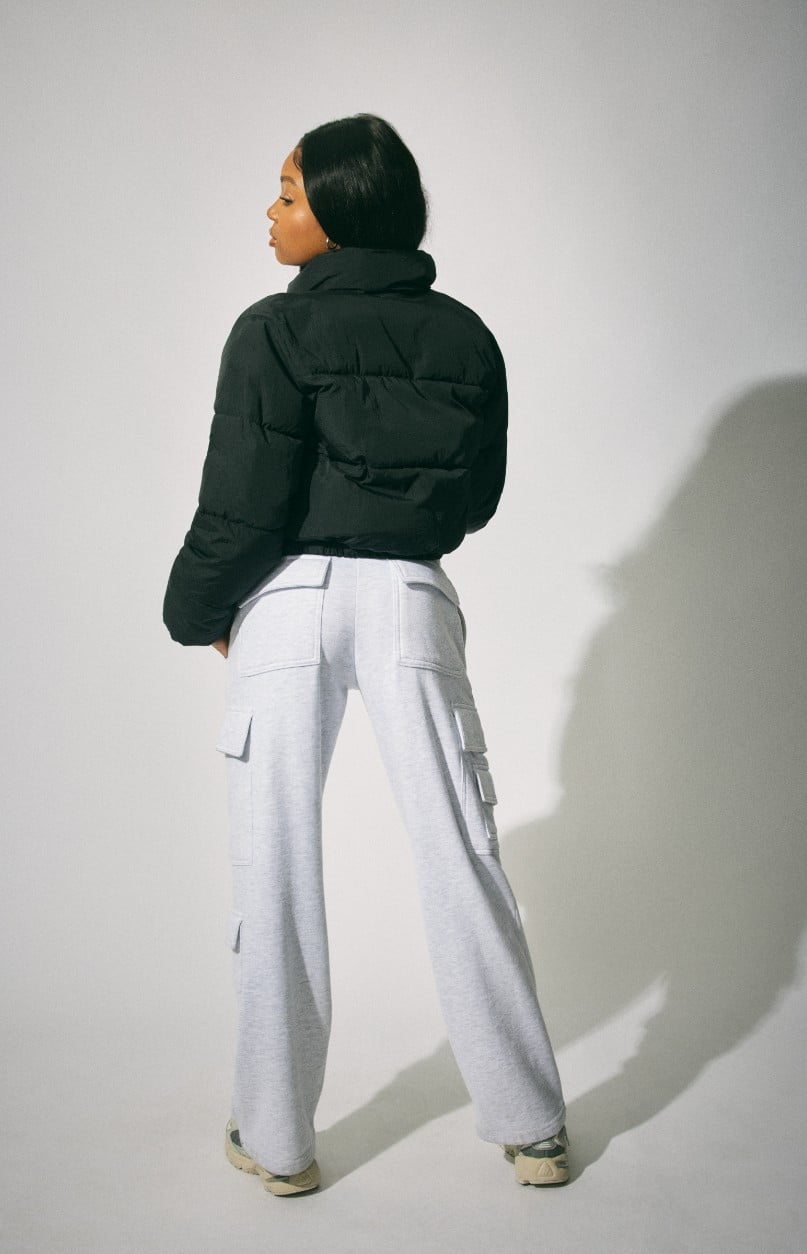 Model wears a black puffer with a cropped black top and grey sweats.