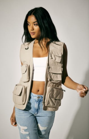 Model is wearing a cargo vest, white tank top, and blue denim.