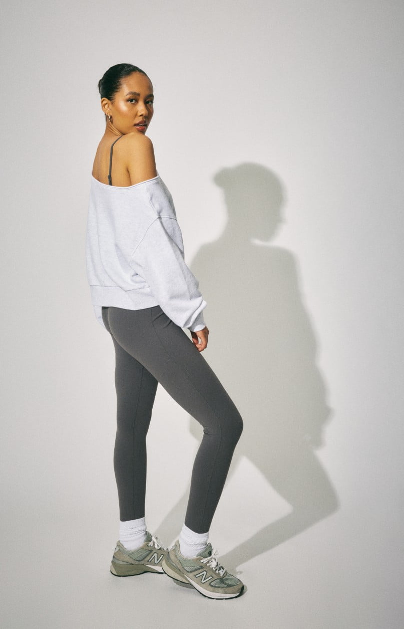 Model wears a grey off the shoulder sweater and black sweats.