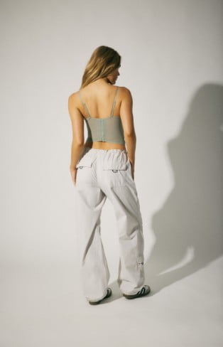 Model is wearing a corset, and grey parachute pants.