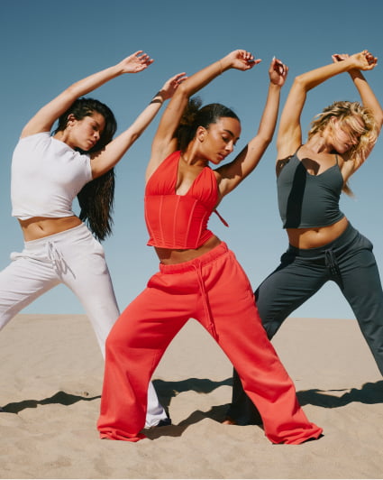 Three models pose in matching outfits, one in grey, one in dark grey, and the last in orange.