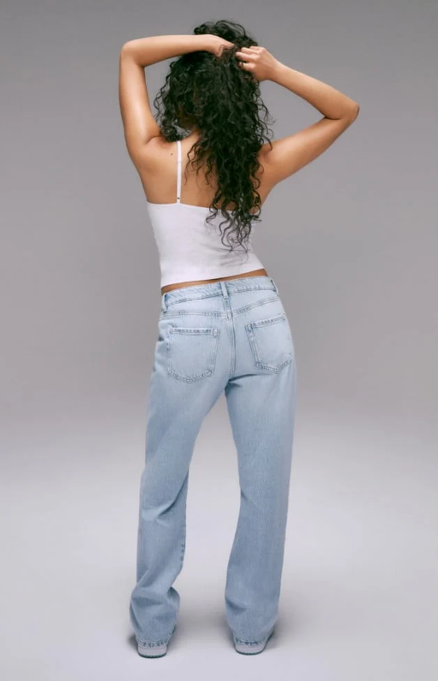Model is wearing white camisole and a light wash low rise denim.