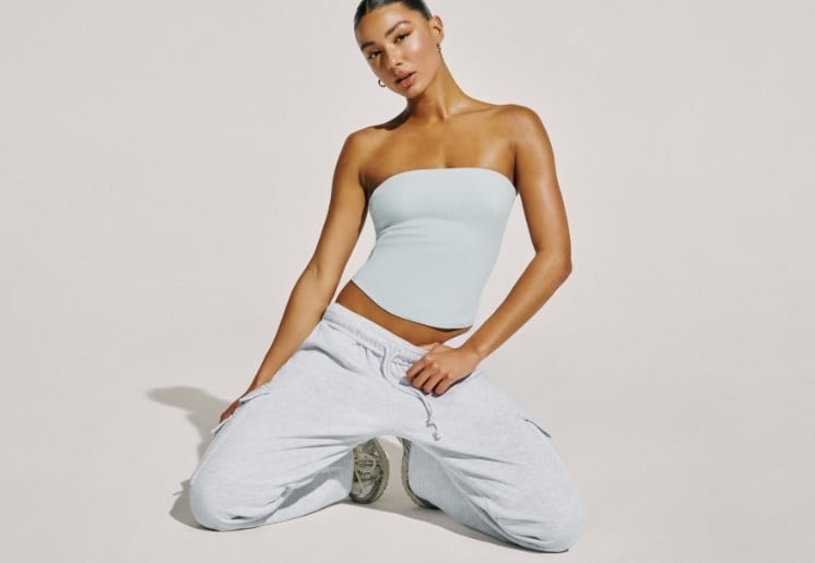 Model poses on a bench wearing light grey cargo joggers and sneakers. 