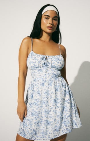 Model is wearing a white tank top mini dress with a light blue floral print.