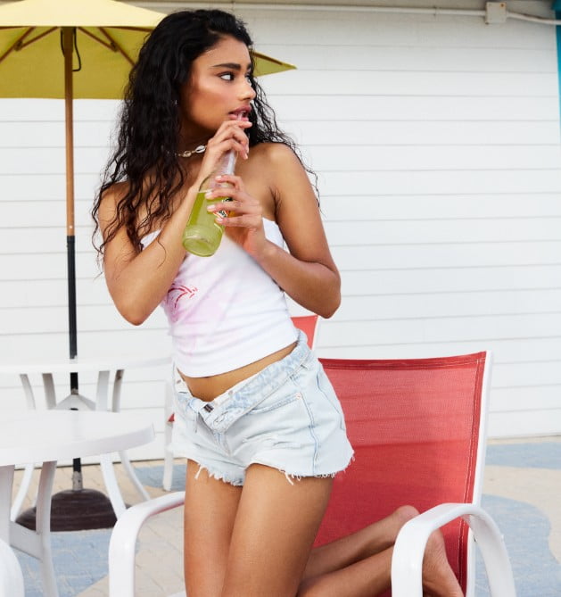 Model poses in a tank top and light wash denim shorts.